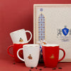 Set of red and white mugs with gold emblem in front of a decorative box on a red background