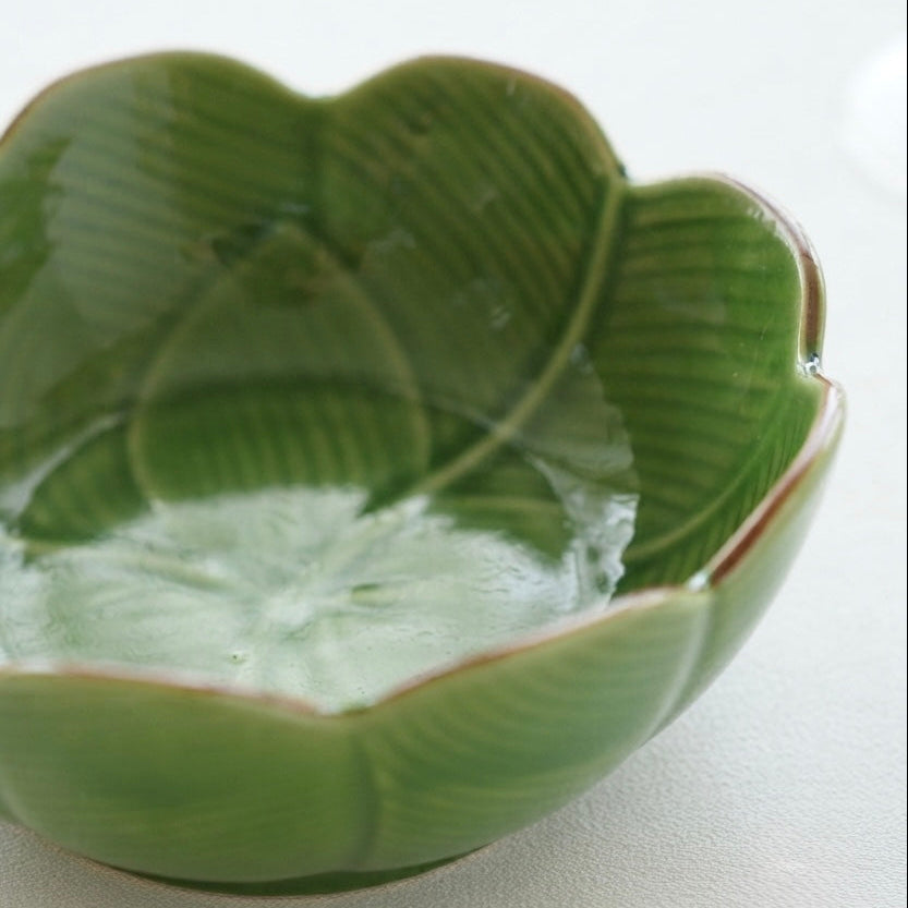 A green ceramic bowl with a petal design and leaf vein detailing, shown on a plain light background.