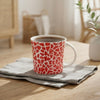 A ceramic mug with a red and white cracked-glass pattern sits on a folded gray napkin on a light wood table in a bright, modern living room setting.