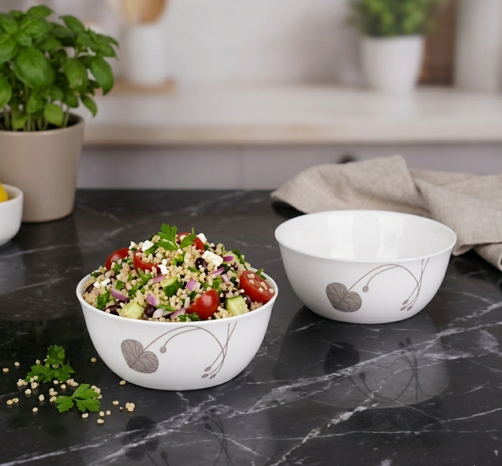 Two white bowls with salad on a dark marble countertop, with a blurred kitchen background.