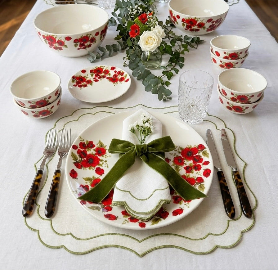 A beautifully set dining table featuring a coordinated red floral porcelain tableware collection, including plates, bowls, and cups, styled with a green velvet napkin and bow, silver cutlery, and a green and white runner.