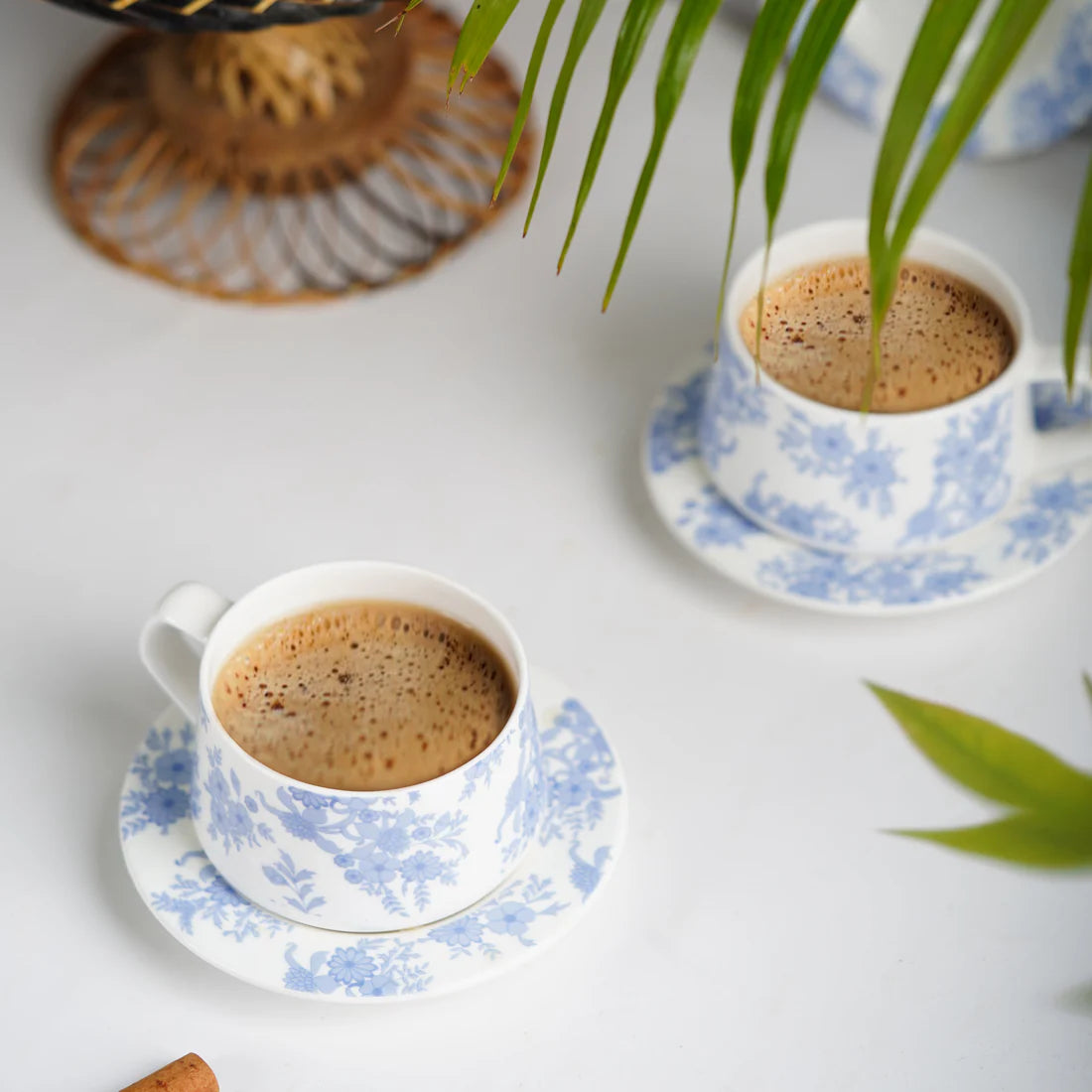 Two cups of coffee on floral saucers with a blurred background