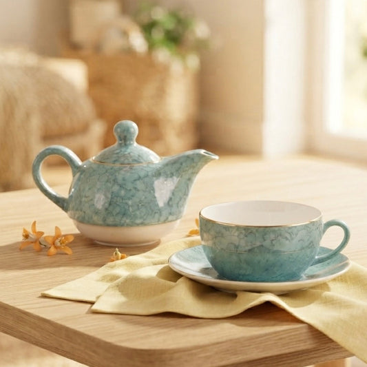 A light blue and white speckled ceramic teapot and matching cup and saucer set, styled on a wooden table with a yellow napkin in a warm, softly blurred indoor setting.