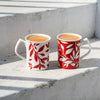 Two bone china mugs filled with coffee, decorated with red and white leaf patterns.