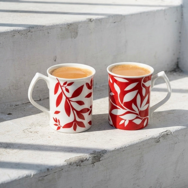 Two bone china mugs filled with coffee, decorated with red and white leaf patterns.