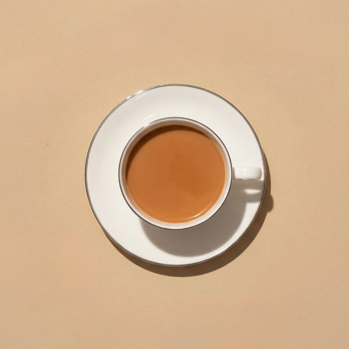 A top-down view of a white ceramic coffee cup and saucer filled with a light brown beverage, set against a solid beige background.